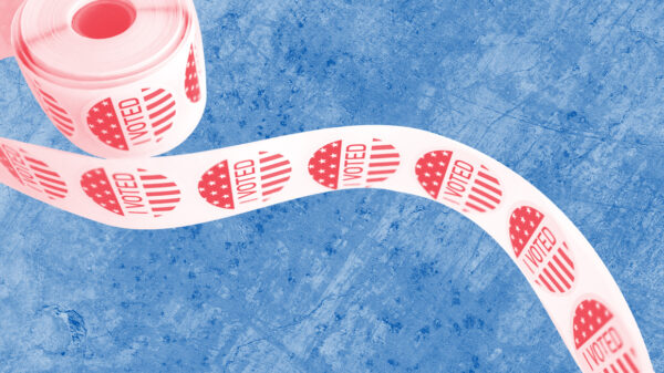 Spool of 'I Voted' stickers with a red and white color overlay on a textured blue background