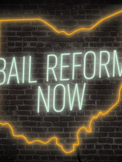 Bail Reform Now neon sign with the ourline of ohio in green and orange on a dark brick background