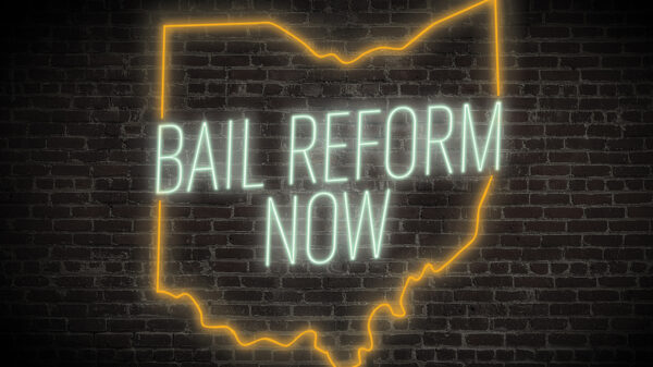 Bail Reform Now neon sign with the ourline of ohio in green and orange on a dark brick background
