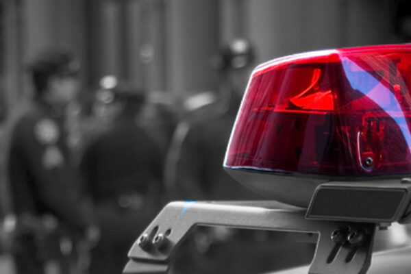 Photograph of a police siren, with police officers in the background depth of field
