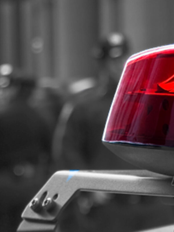 Photograph of a police siren, with police officers in the background depth of field
