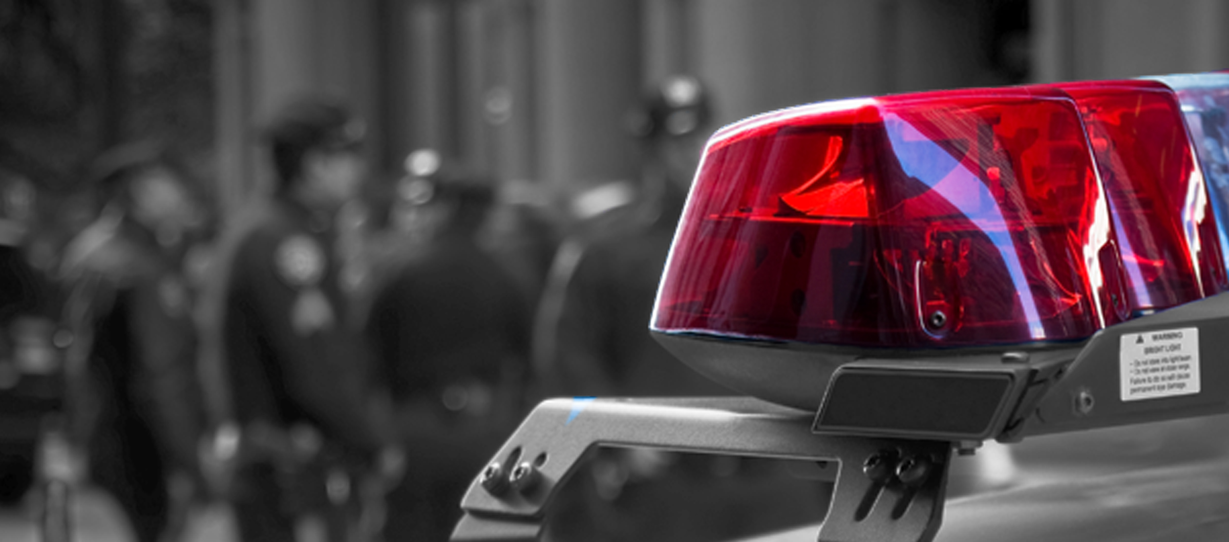Photograph of a police siren, with police officers in the background depth of field