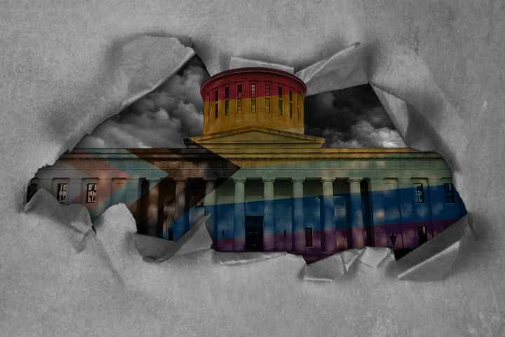 Ohio Statehouse with a pride flag overlay, with dark clouds in the sky, and tearing through paper