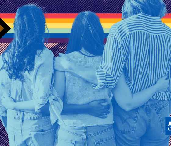 Image of three young people with their arms around each other and an LGBTQ+ pride flag in the background